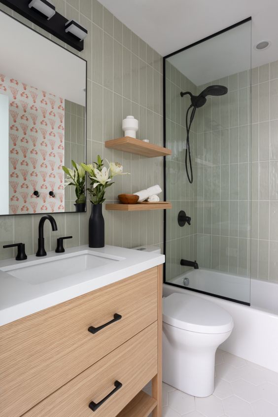 a small modern bathroom with light green tiles, a stained vanity, black fixtures, a mirror and open shelves