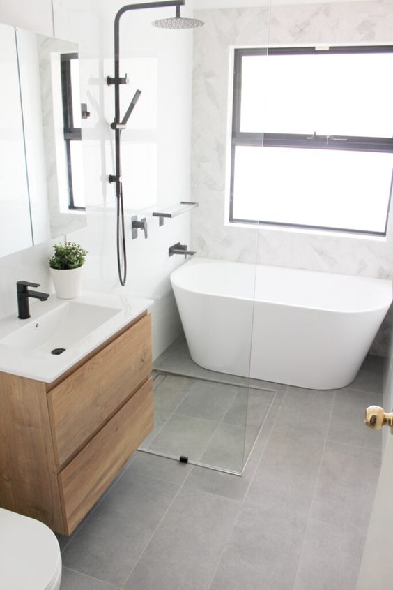 a small modern bathroom with white marble and grey stone tiles, a stained vanity, an oval tub, black fixtures