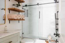 a small modern bathroom with white subway and hex tiles, a bathtub with a shower, a mint colored vanity, open shelves and a stool