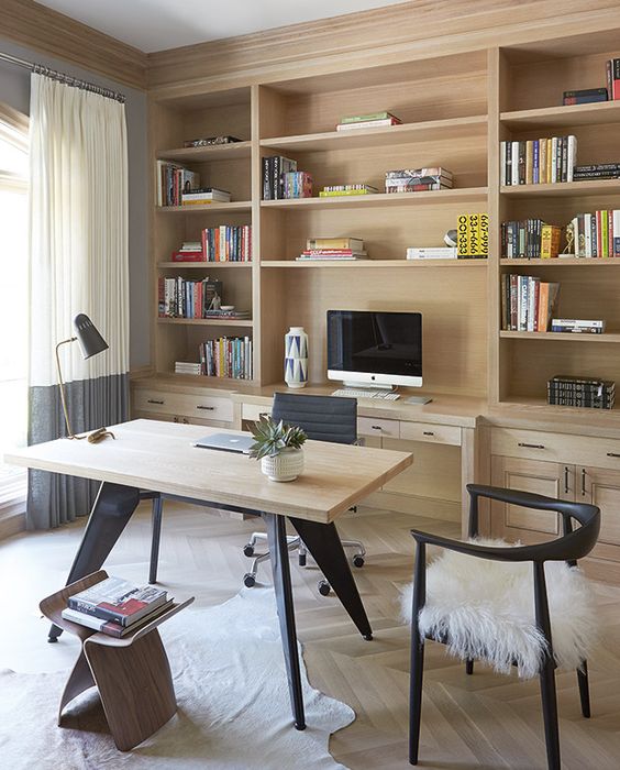 A small modern home office with a built in storage unit, a desk, black chairs, books and a PC