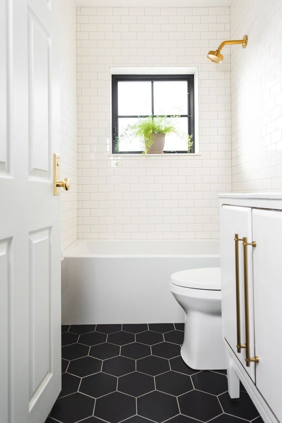 a small yet cool bathroom done with white subway tiles and black hex ones, gold touches and potted greenery is a lovely space