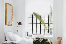 a small yet very chic bedroom with a bed, a mirror in a gilded frame, a nightstand, a chair, some books and pretty bedding