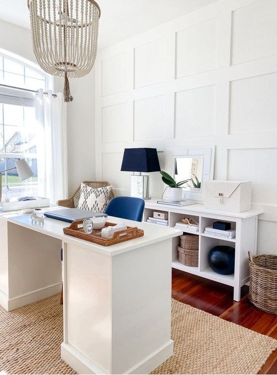 a stylish beach home office with white paneling, white furniture, navy accents, baskets and a wooden bead chandelier is gorgeous