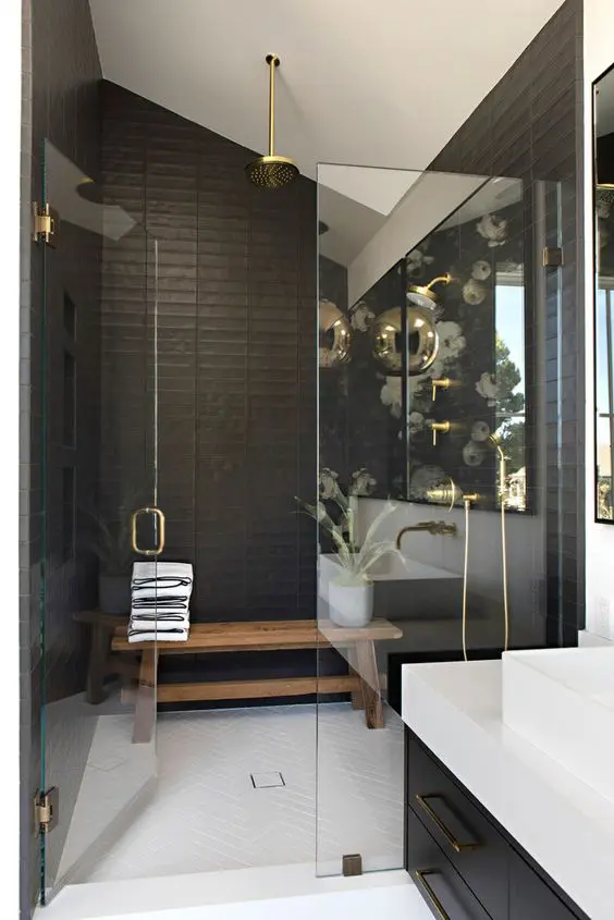 a stylish black and white bathroom with a shower space, a bench, gold fixtures, a black vanity and a white stone countertop