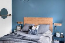a stylish contemporary bedroom with a blue accent wall, navy nightstands, grey and navy printed bedding and a geometric lamp
