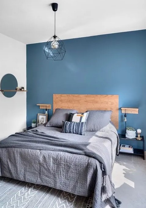 a stylish contemporary bedroom with a blue accent wall, navy nightstands, grey and navy printed bedding and a geometric lamp