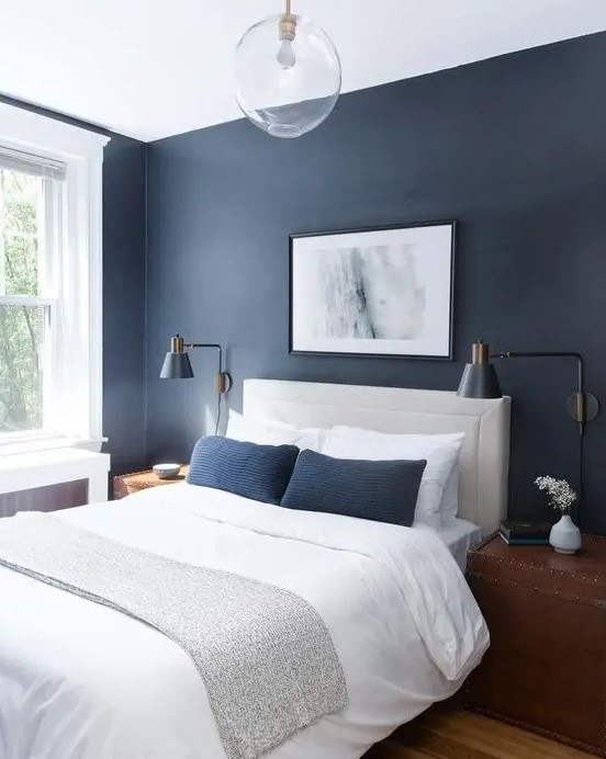 a stylish contemporary bedroom with navy walls, a white leather bed, wooden chests as nightstands and navy pillows