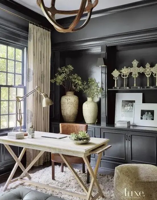 A stylish home office with black walls, black storage units, a light stained desk and a brown chair, a wooden sphere chandelier