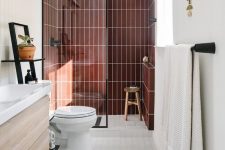 a stylish mid-century modern bathroom with a shower space with burgundy tiles, a stained vanity, a boho rug and black fixtures