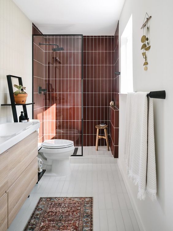 a stylish mid-century modern bathroom with a shower space with burgundy tiles, a stained vanity, a boho rug and black fixtures