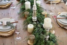 a stylish rustic Christmas table with an evergreen runner, candles, wooden placemats, cinnamon sticks and gold cutlery