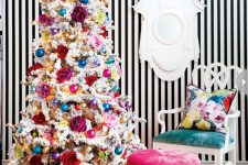 a super bright glam Christmas decor with a white tree with bold ornaments, flowers, lights and colorful gift boxes around