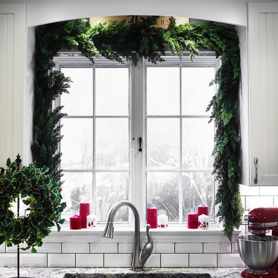 a super lush evergreen garland framing the window instantly brings a holiday feel to the space, and red candles add to it