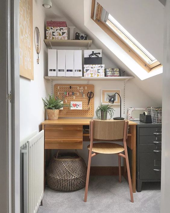 a tiny attic home office with a two-tone desk, a wooden chair, open shelves, some plants, a basket for storage is cozy and cool
