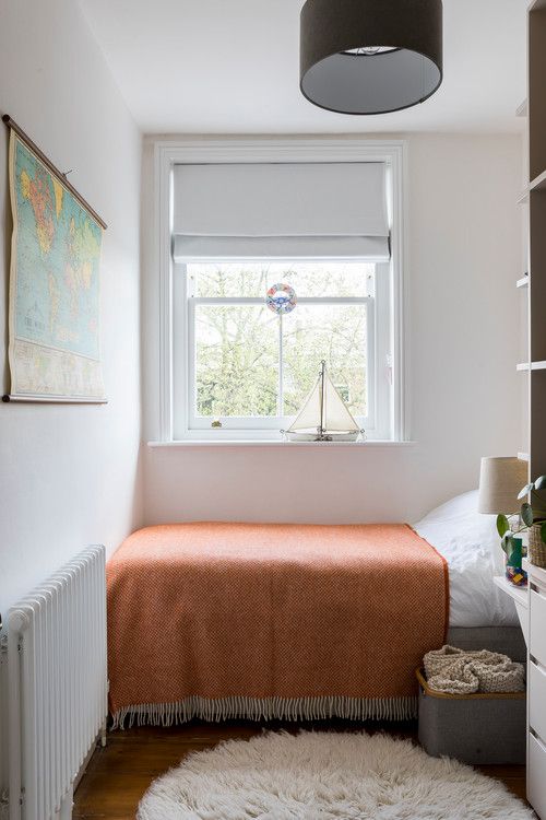 a tiny bedroom with a bed with a rust blanket, a box with blankets, a shelving unit and some decor will do as a guest bedroom or even a kid's room