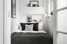 a tiny contrasting bedroom with niches as storage shelves, a bed with contrasting bedding, an artwork and a sconce