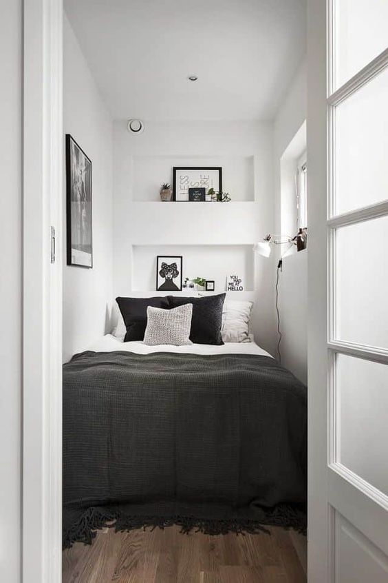a tiny contrasting bedroom with niches as storage shelves, a bed with contrasting bedding, an artwork and a sconce