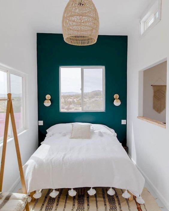 a tiny pretty bedroom with a dark green accent wall, a bed, a printed rug, a woven pendant lamp and a mirror