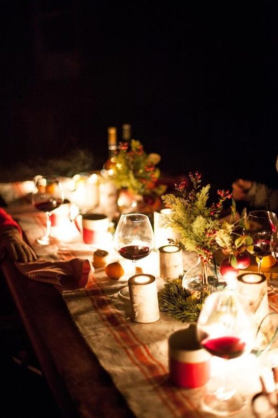 a very cozy and beautiful Christmas tablescape with candles, lights, evergreens, berries and a striped table runner