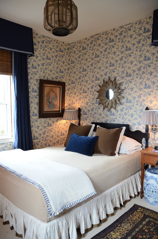 a vintage bedroom with floral wallpaper, a cozy upholstered bed, a pendant lamp, mirrors and artworks is very chic