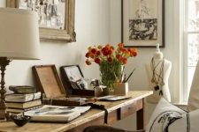 a vintage farmhouse home office with a wooden desk, a refined chair, chic artworks and a table lamp and blooms