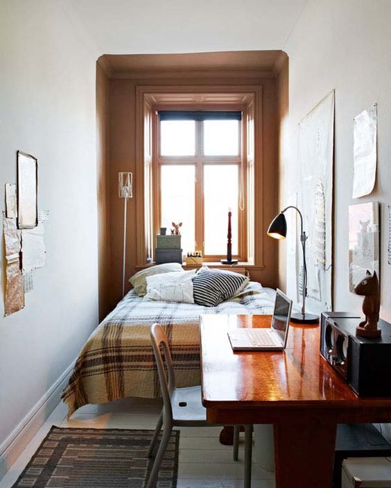 a welcoming small bedroom with a bed and printed bedding, a stained desk and a chair, a table lamp, a gallery wall