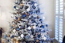 a white Christmas tree with navy, white, silver and blue ornaments, a gold star topper and icicles is very bold