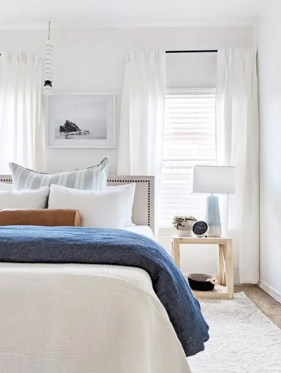 an airy modern beach bedroom with neutral walls, white curtains, blue textiles and lamps, catchy dark items