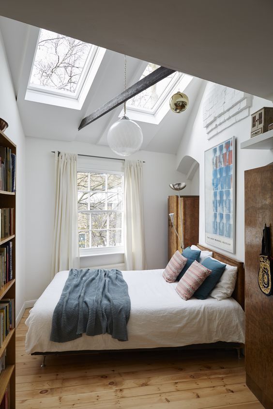 an attic bedroom with a bed, a bookcase, a wardrobe, skylights and some bold bedding and artwork