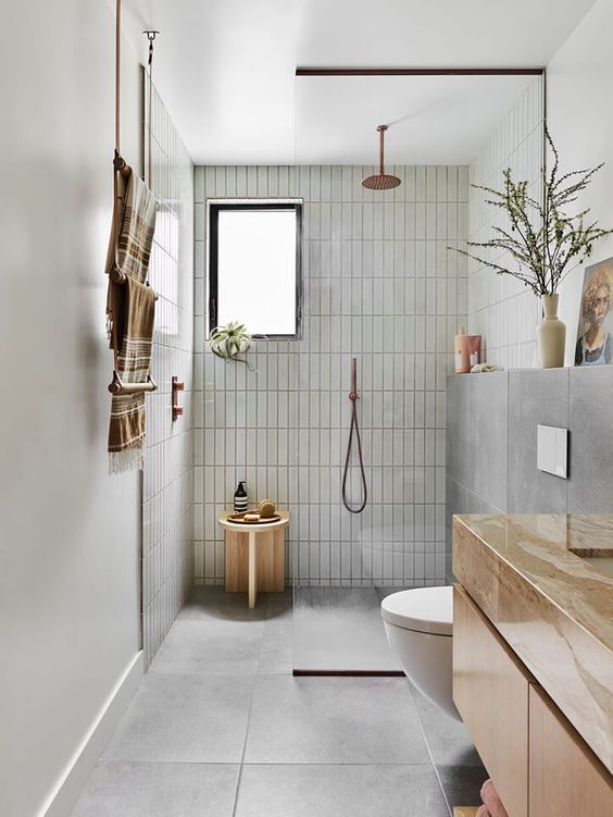 an earthy minimalist bathroom with grey tiles, a shower space with a stool, a floating vanity and rust-colored stone, some decor