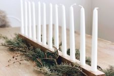 an easy and fast Nordic table centerpiece of a wooden candleholder, candles and fir branches is a very cool and chic idea