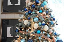 an elegant Christmas tree with navy, blue and green and white ornaments, ribbons, lights and a star topper