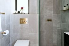 an elegant contemporary bathroom with stone and marble tiles, a window, a shower space and gilded touches