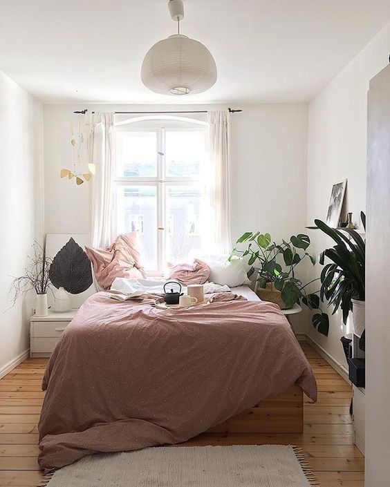 an elegant small bedroom with stylish furniture, mauve and white bedding, a white lamp and potted plants