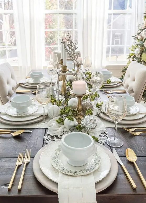 an ethereal Christmas tablescape with neutral and metallic ornaments, neutral porcelain, greenery, candles and white porcelain