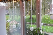 an evergreen garland with lights, pompoms and ornaments hanging down is a cool window decoration