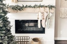 chic Scandinavian mantel decor with greenery, wooden beads, neutral stockings and neutral tinsel Christmas trees