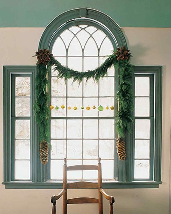 decorate a window wit an evergreen Christmas garland, colorful ornaments and large pinecones to make it cooler