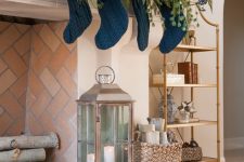 elegant blue Christmas decor with a fir garland with lights, berries, navy stockings and navy cushions at the fireplace