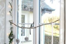 hanging silver snowflakes, a fir garland, lights, silver glitter pinecones on ribbns and silver glitter candles to decorate the window in snowy fairy-tale style