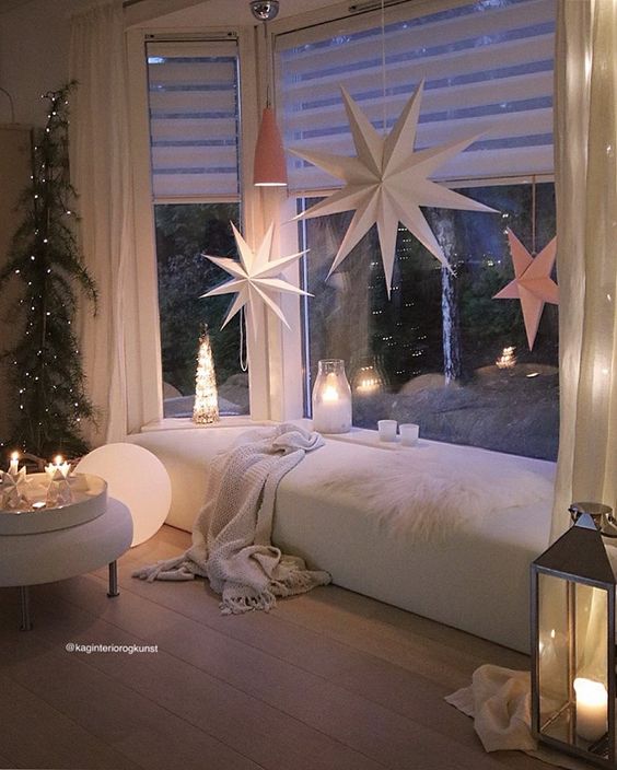 large paper stars hangong on the bow window, lanterns and a Christmas tree on the side to create a cozy space