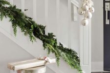 lovely Christmas staircase decor with a lush greenery garland and lots of white bells attached to it is chic and simple