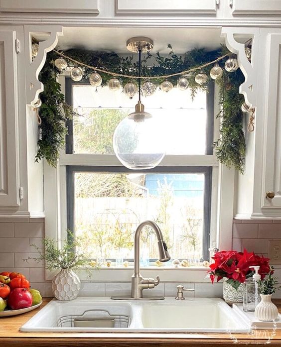 lovely Christmas window decor with evergreens and a garland of vintage ornaments is a cool idea