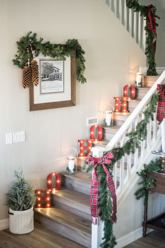 lovely farmhouse Christmas staircase decor with marquee letters, candle lanterns, evergreen garlands and plaid bows, pinecones and a mini tree