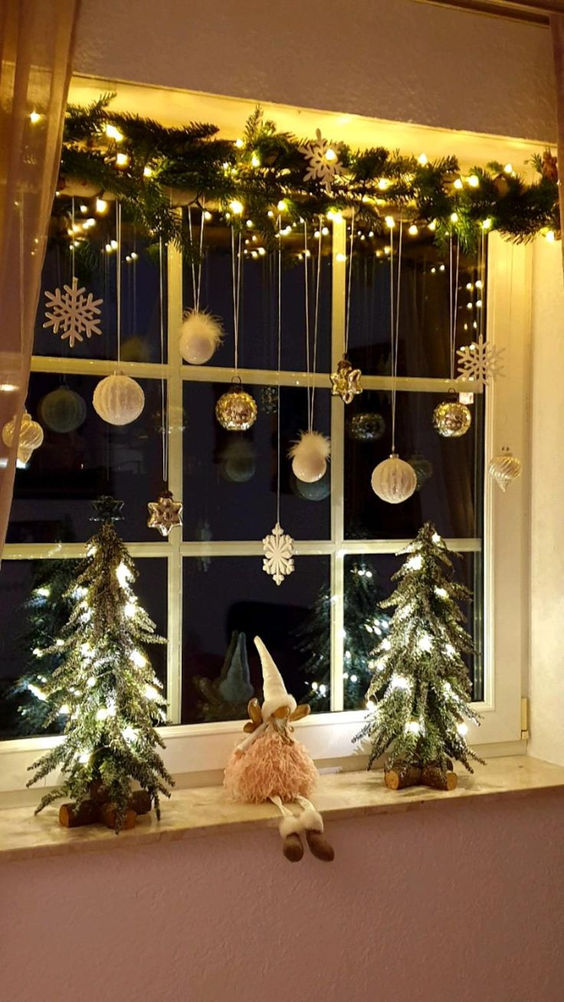lovely holiday window decor with silver and white ornaments, evergrees and lights is amazing