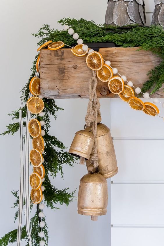 natural Christmas mantel decor with a fir garland, dried citrus, pompoms and large vintage bells is very chic and beautiful