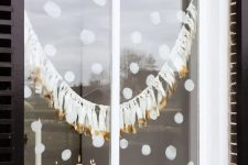 painted snowballs and a tassel garland are a cool way to style a window for the holidays
