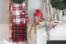 plaid scarves, mittens and a fir wreath and lights on the ladder, branches, berries and a red lantern on the mantel feel very rustic