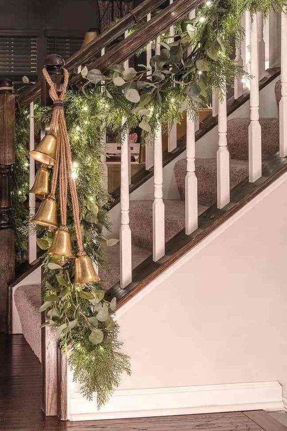 railings decorated with a greenery and fir branch garland, with lights and large vintage bells will make your space feel Christmassy