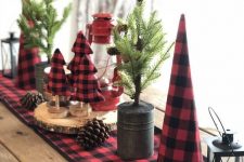 rustic Christmas table decor with a plaid runner and plaid felt trees, pinecones, a red lantern and mini trees in buckets